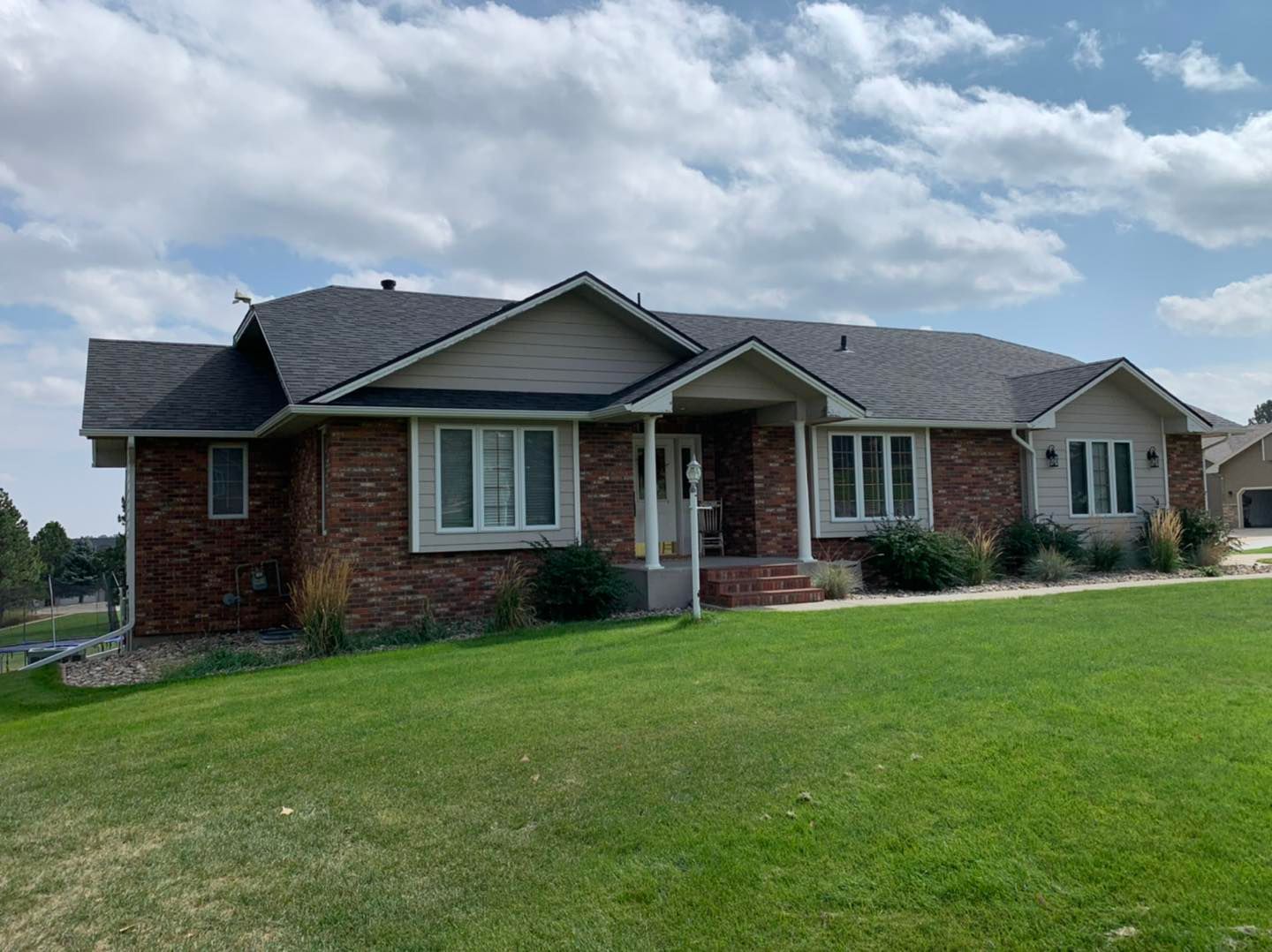 Brick ranch-style house with green lawn under cloudy sky.