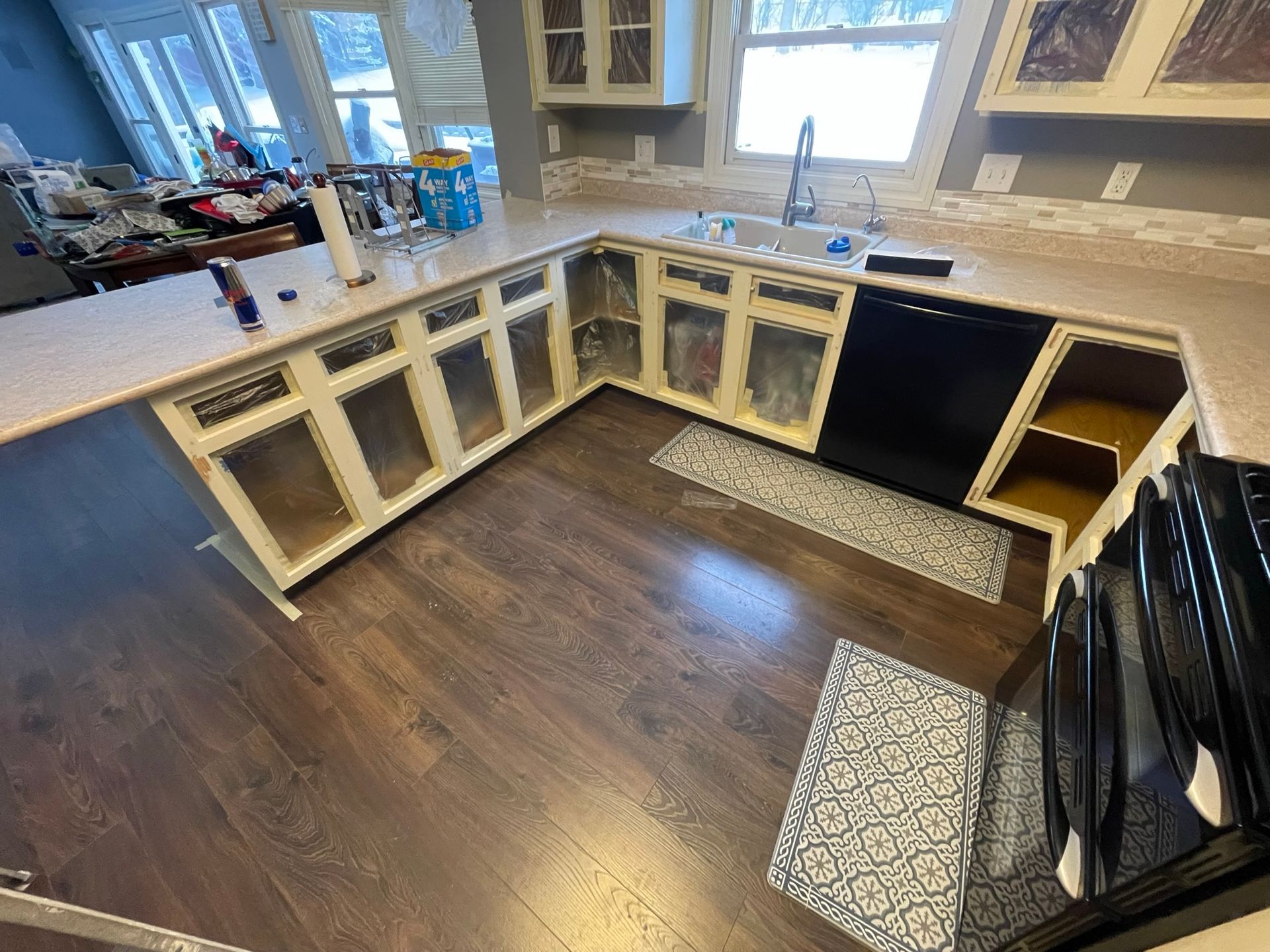 Kitchen remodel in progress: cream cabinets, dark wood floor, white countertops, black dishwasher.