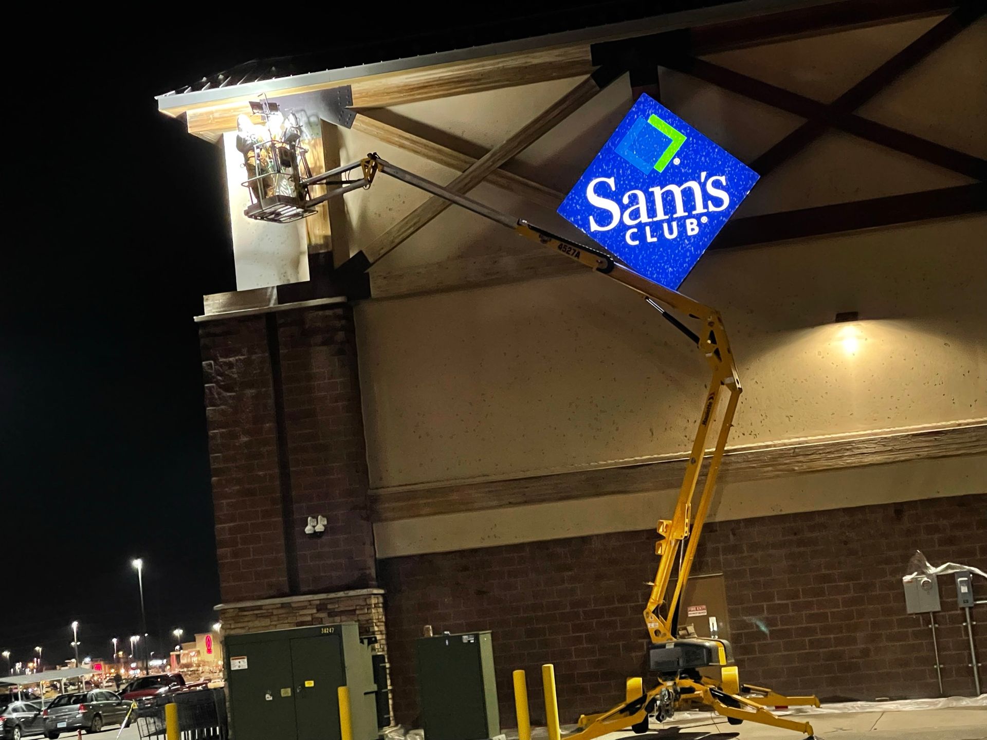 A worker on a lift installs a Sam's Club sign on a building at night.