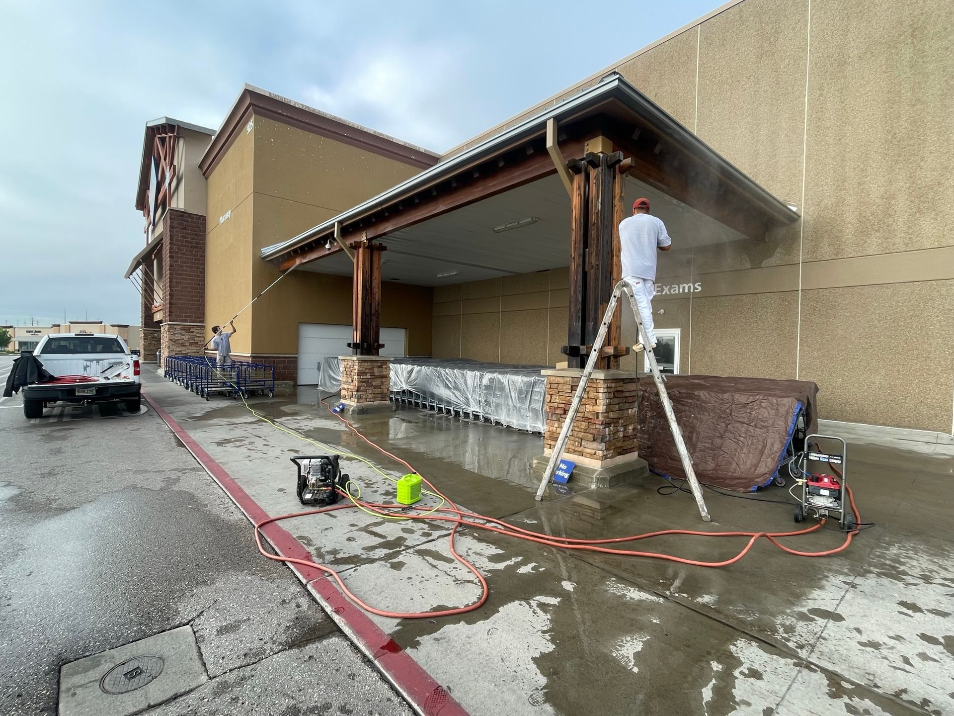 Men pressure washing a building exterior. Water on pavement.