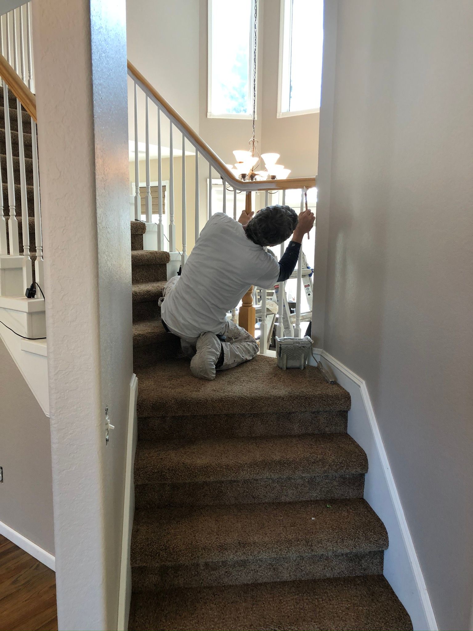 Person working on stairs, installing something, inside a house. Stairs are carpeted, walls are light gray.