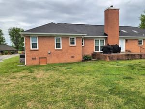 Brick house with dark roof and tall chimney, back view in a grassy yard.