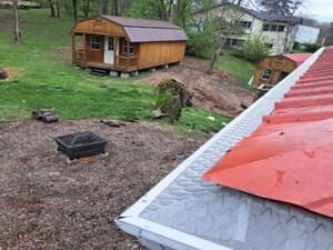 Red roof in foreground; wooden shed on a hill with green grass in the background.