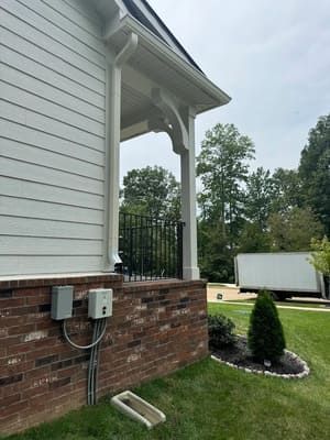 Side view of a house with white siding, a brick base, and a porch supported by white columns.