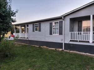 Gray house with porch, windows, and shutters, set in a grassy yard under a dusky sky.