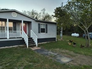 Gray house with porch, chickens in yard, and propane tank.