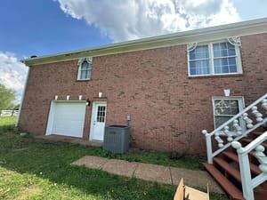 Brick building with garage, door, and windows under cloudy sky.