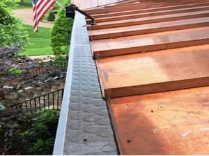 Copper roof with a metal gutter and the American flag in the background.