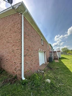 Red brick building with white gutters and downspout. Sunny outdoor setting.