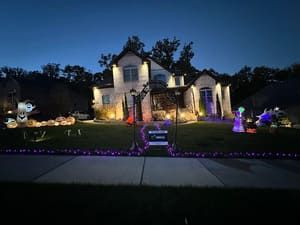 Halloween-decorated house at dusk with purple lights along the lawn and various spooky decorations.