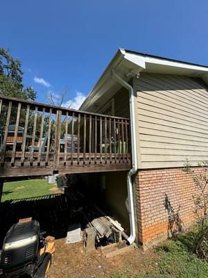 Wooden deck attached to a house with beige siding and brick foundation. Gutters and a boat visible.
