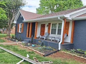 Blue house with white trim, brown shutters and porch posts, and brown roof.