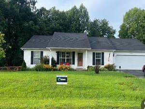 White house with black shutters, green lawn, trees in background, and a 