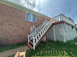 Brick building with white lattice deck, stairs, and railing. Brown steps. Blue sky.