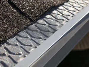 Gutter guard installed on a roof with asphalt shingles. The guard has a leaf-like pattern.
