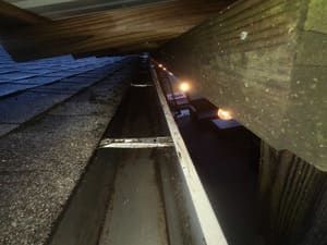 Inside a gutter, looking up at the roof and wooden beam. Shingles on the roof are visible.