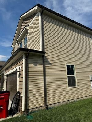 Beige siding on a two-story house with dark brown trim and gutters, and a garage door.