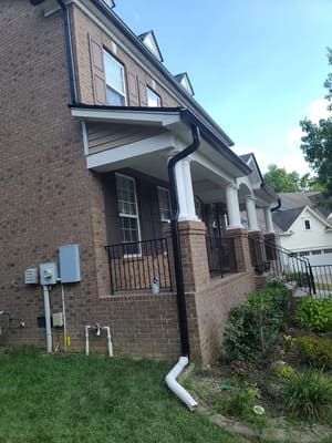 Brick house with black gutters, white porch, and green lawn.