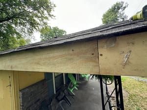 Close-up view of a roof’s edge with weathered wood trim. Overcast day. Green chairs visible underneath.