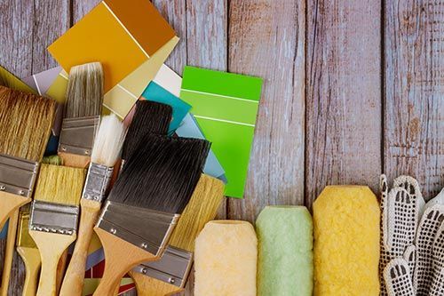 A bunch of paint brushes and paint rollers on a wooden table.
