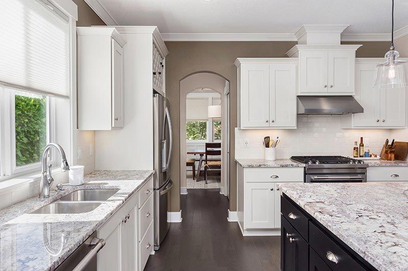 A kitchen with white cabinets , granite counter tops , and stainless steel appliances.