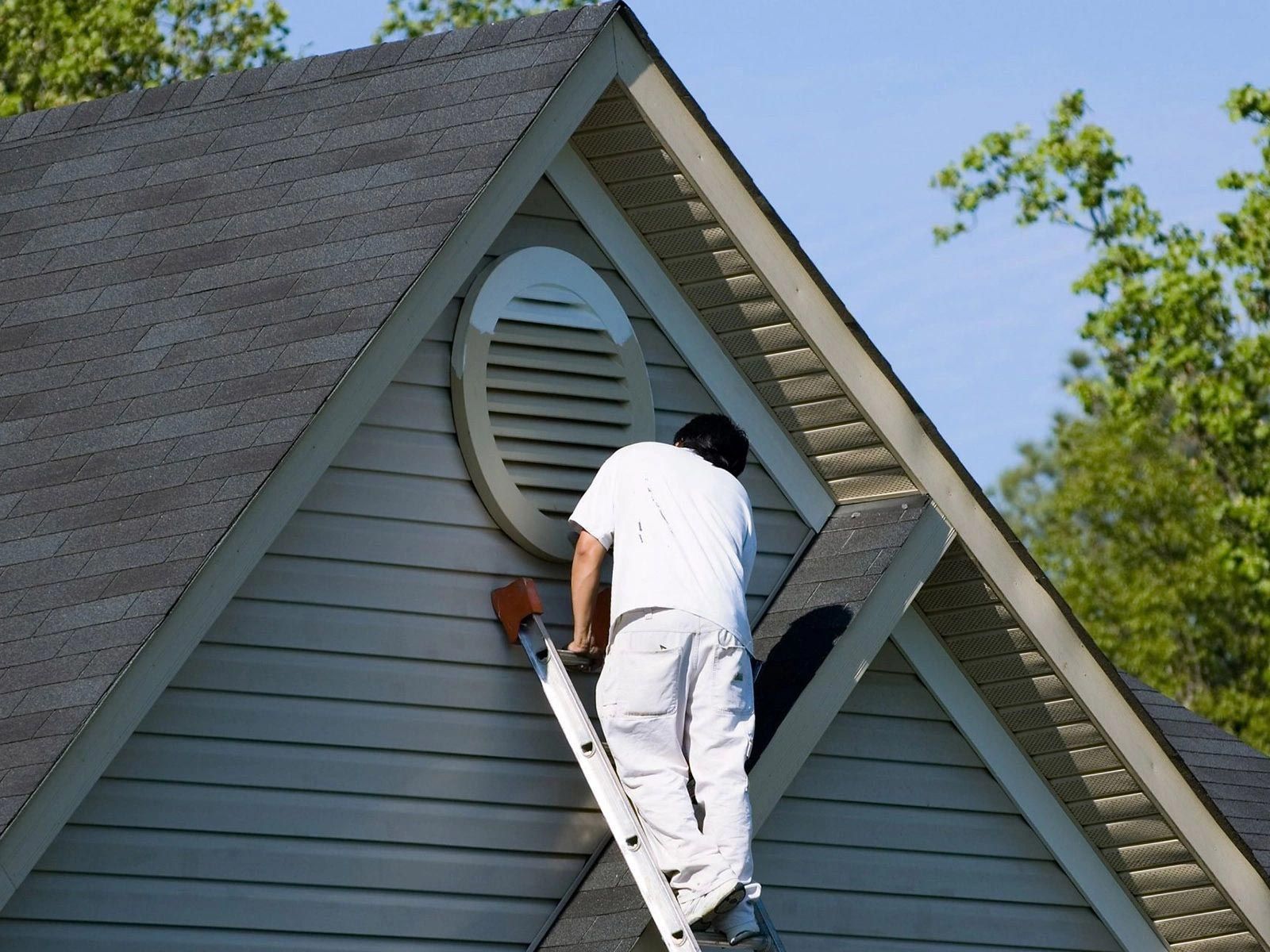 A man on a ladder paints the side of a house