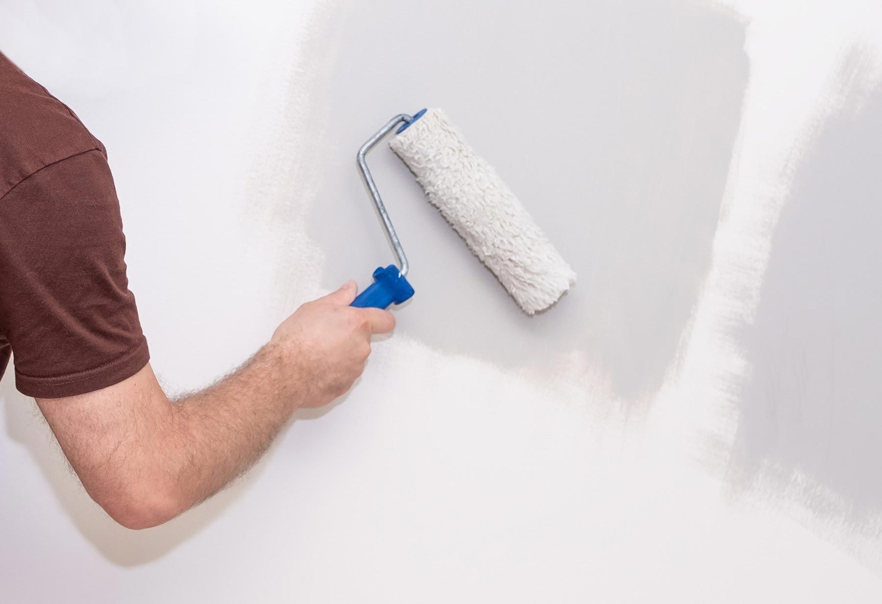 A man is painting a wall with a paint roller.