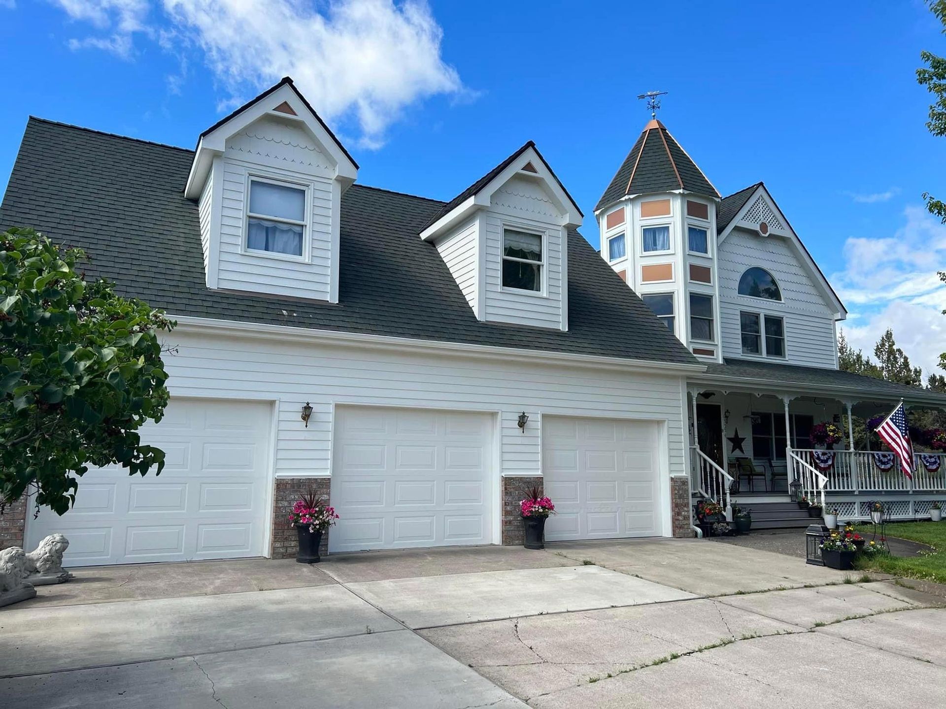 A large white house with a black roof and three garage doors.