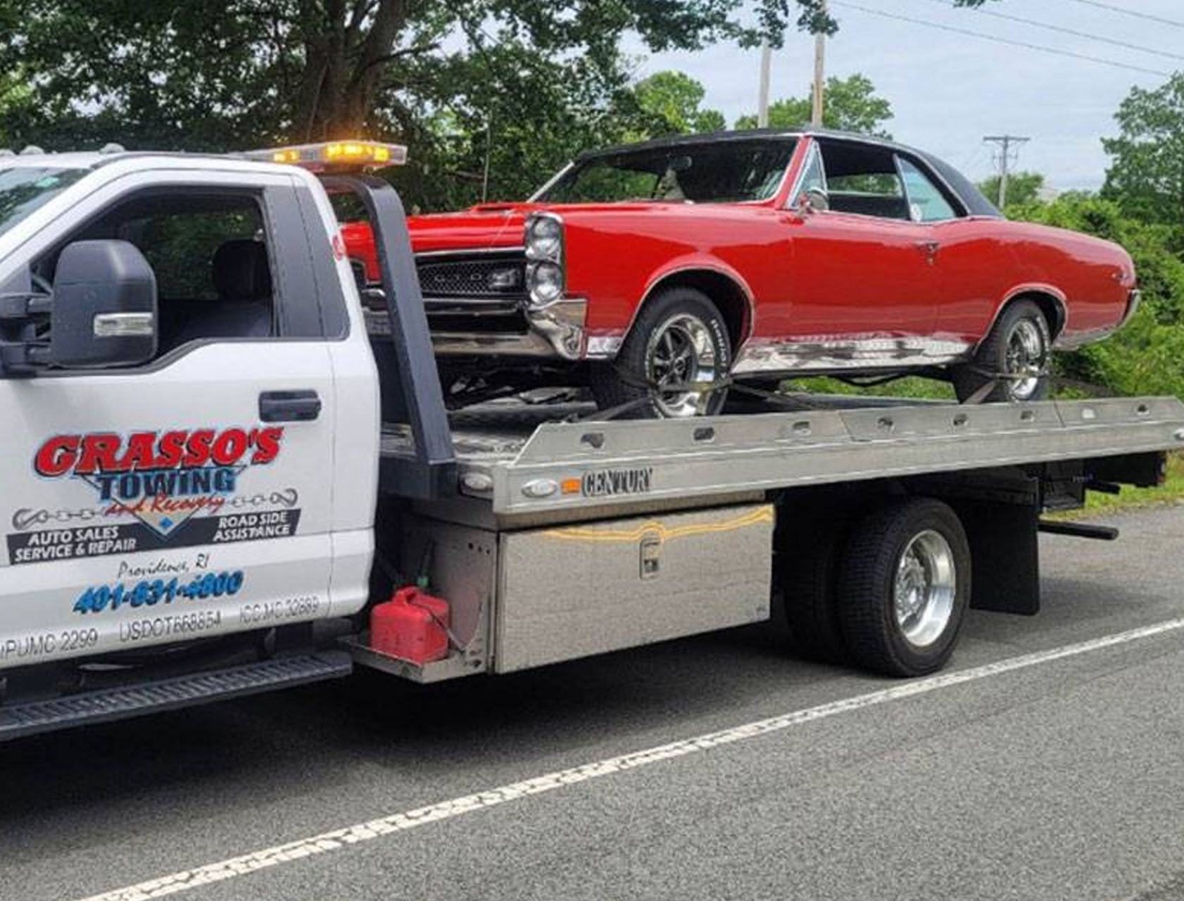 Tow truck hauling a red classic car on a flatbed along a roadside