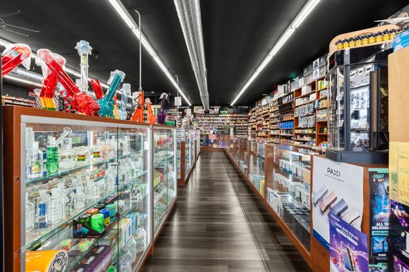 Interior of a shop with glass display cases filled with smoking accessories; dark wood floors and ceiling.