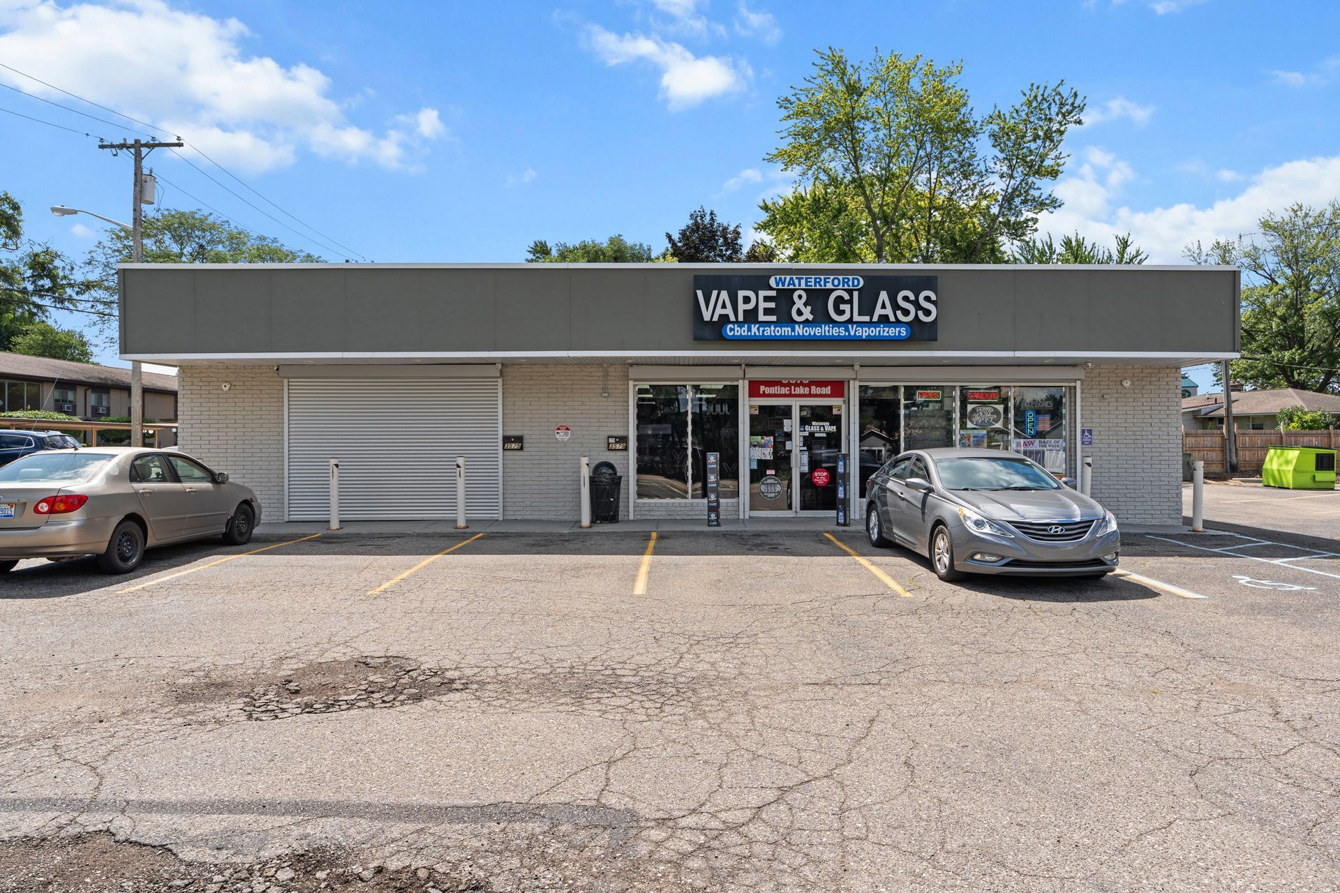 A vape and glass shop with cars parked out front on a sunny day.
