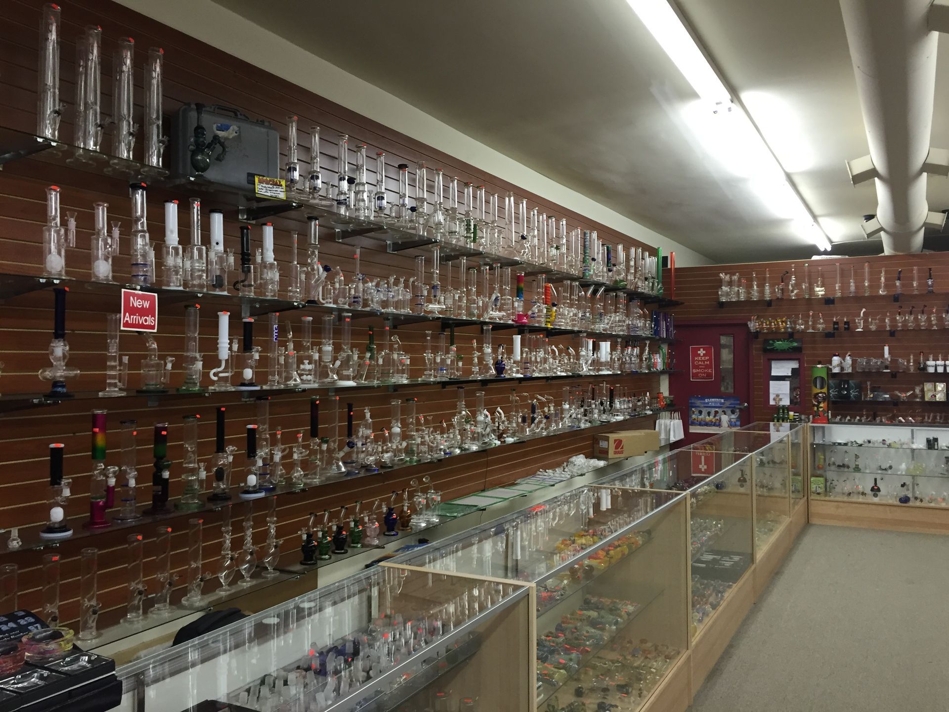 Inside a glass shop: shelves display various glass bongs, pipes, and related items. Shop is well-lit.