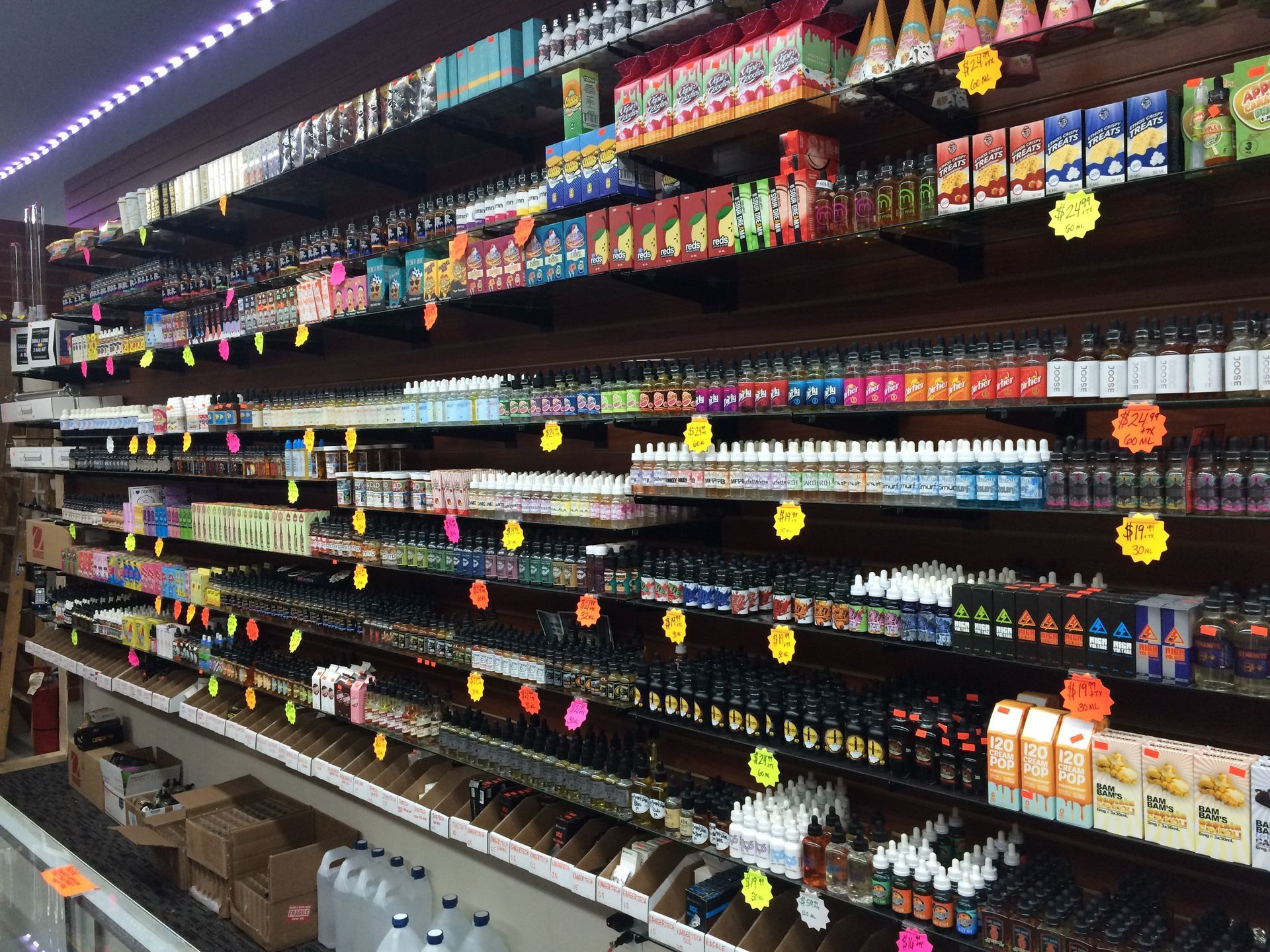 Shelves stocked with various vape products in a shop. Price tags and colorful bottles are visible.