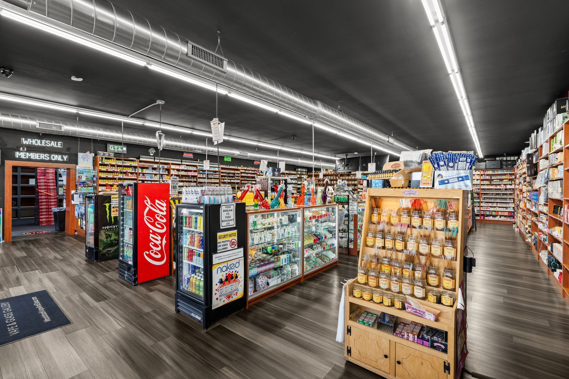 Inside a store: aisles of books, candy displays, Coca-Cola sign, wood floors, and bright lights.