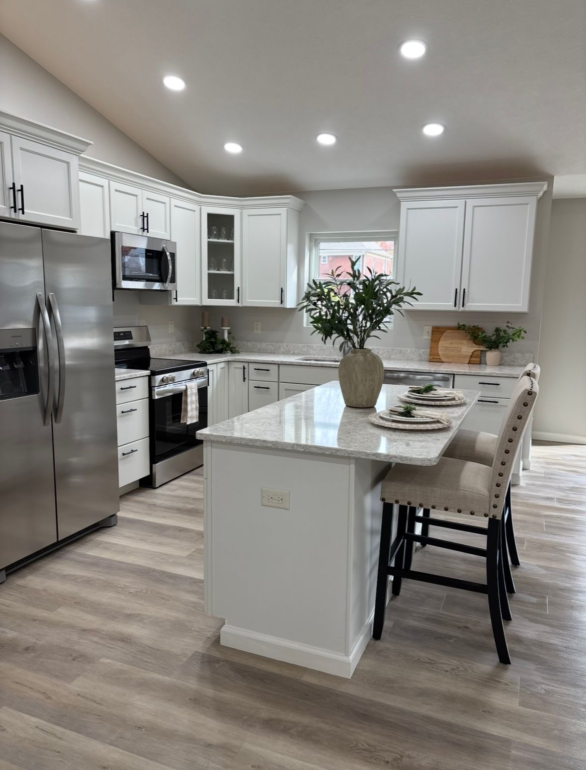 Modern kitchen with white cabinets, stainless steel appliances, a marble-topped island with two stools, and wood flooring.