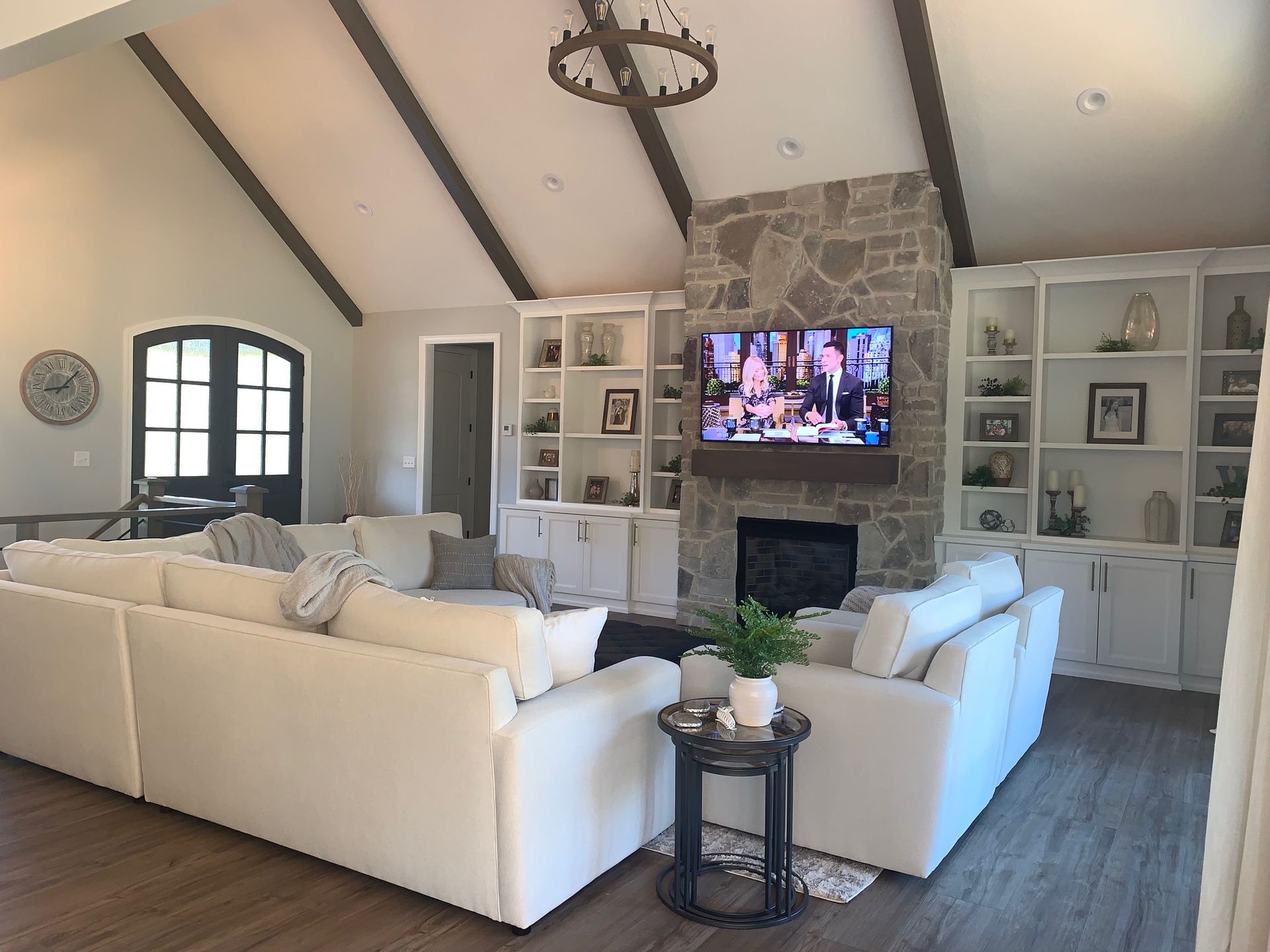 A spacious, modern living room featuring a large white sectional sofa, a stone fireplace with a TV, and built-in shelves.