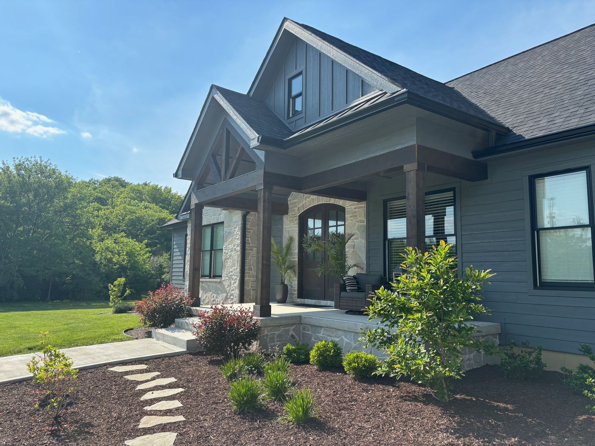 A modern farmhouse with grey horizontal siding, stone accents, a dark wood-pillared porch, and a stone walkway.