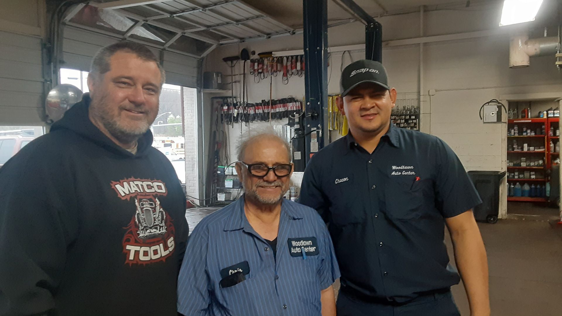 Three men smiling in a workshop, standing together near tools and equipment.