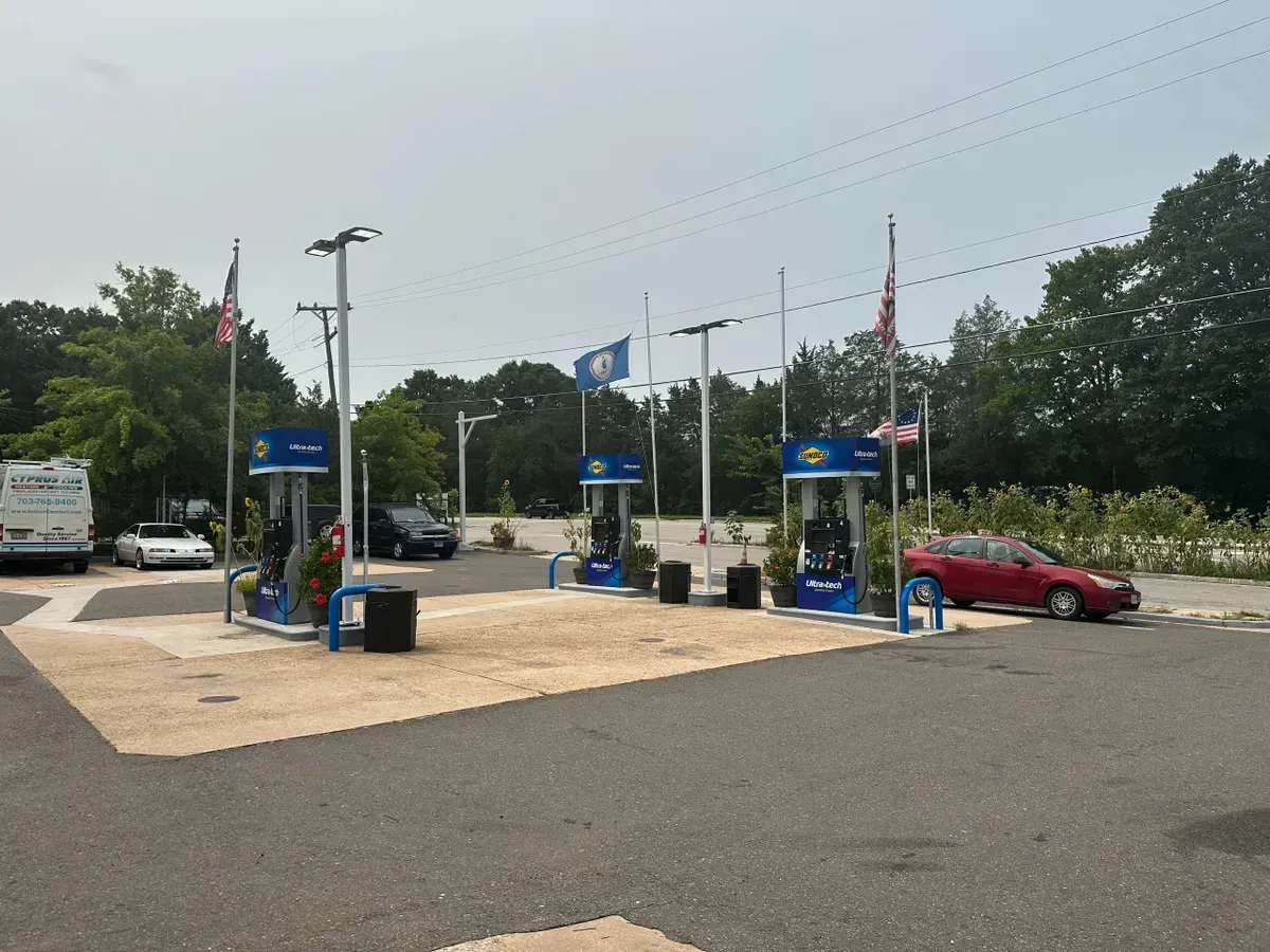 Outdoor parking lot with EV charging stations, blue signs, and a red car nearby under cloudy skies