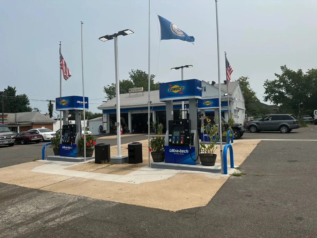 Gas station pumps under blue canopies with flags, on a paved lot under a gray sky