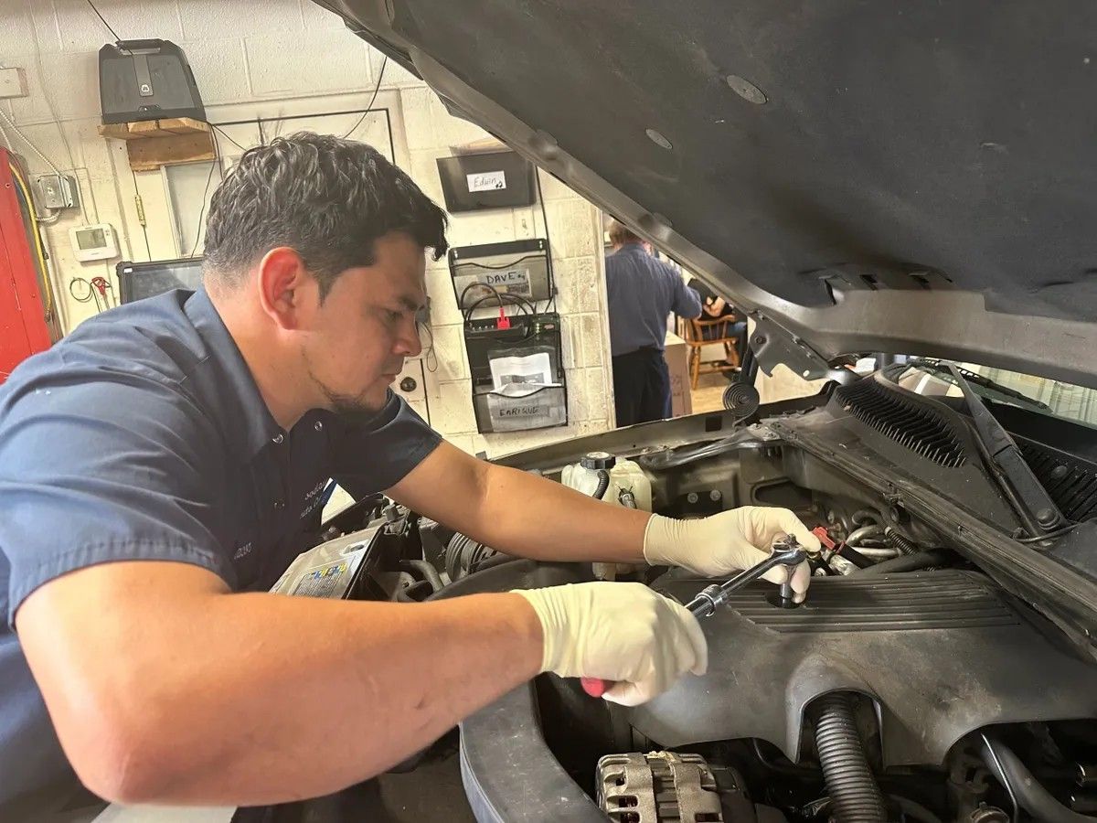 Mechanic in blue shirt and gloves working under an open car hood in a garage