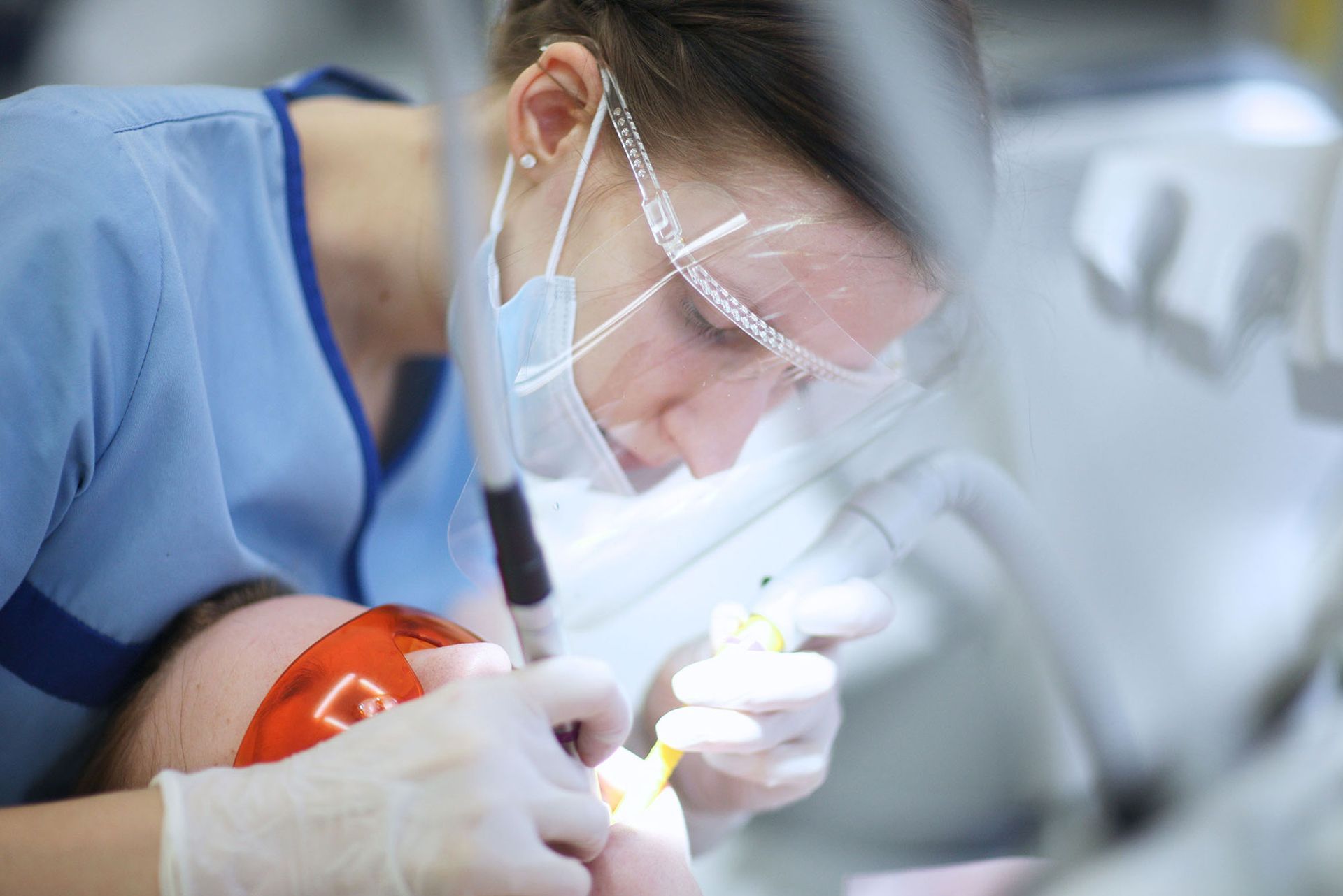 Dentist using tools on a patient in a dental chair. Both are wearing protective eyewear.