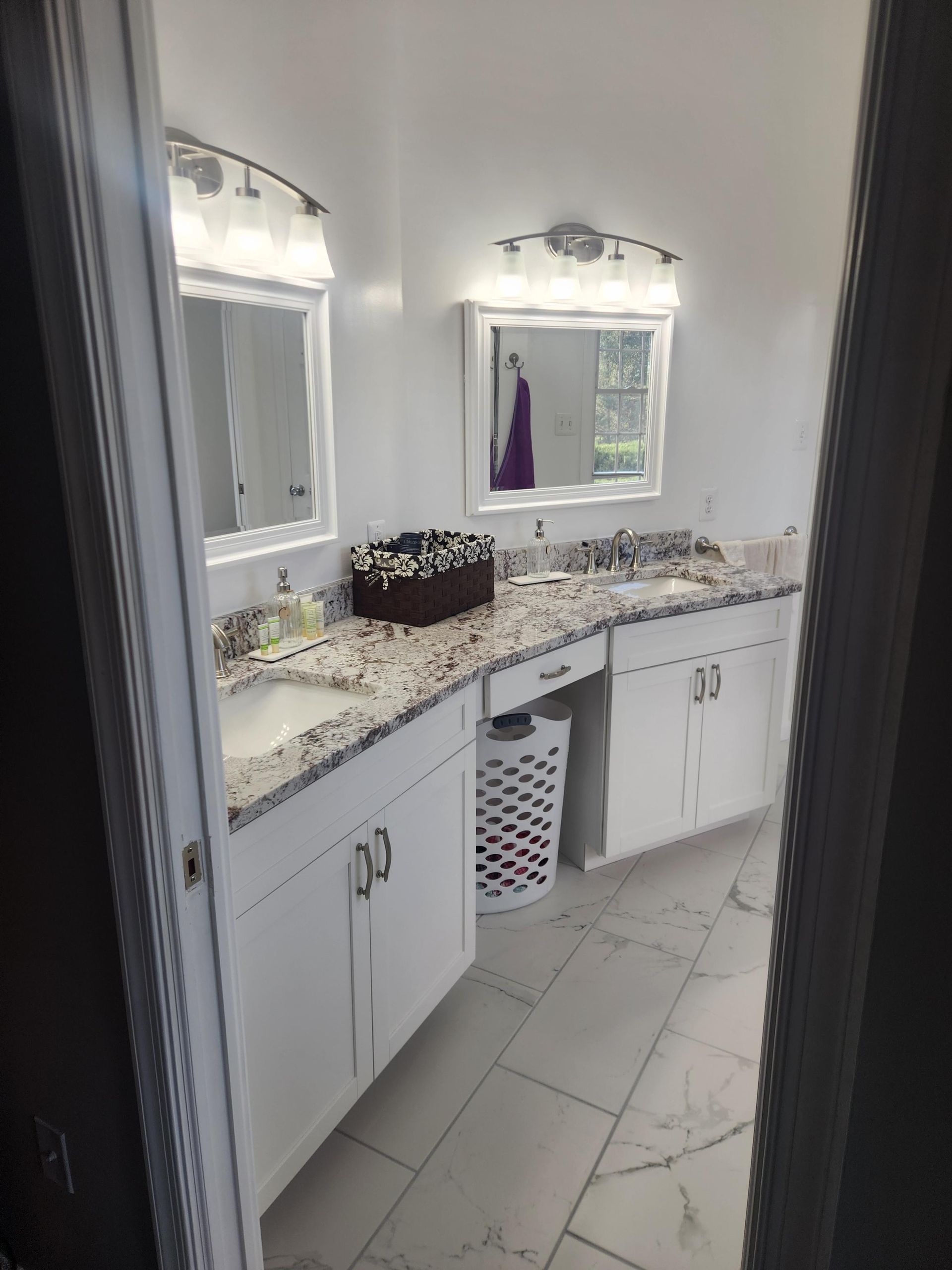 A bathroom features a double vanity with white cabinets, granite countertops, two mirrors, and overhead lighting.