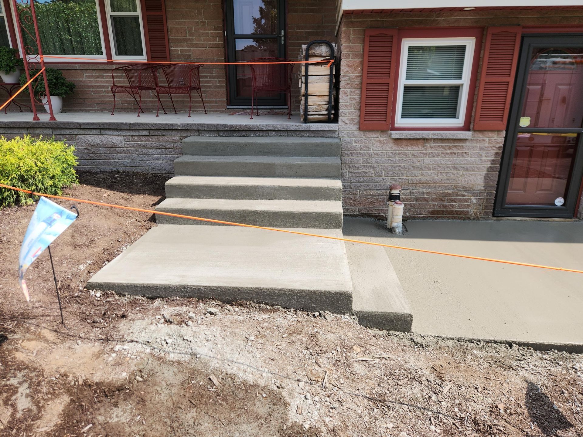 Newly poured concrete steps and a walkway leading to the front entrance of a brick house.