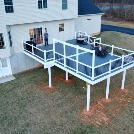 An elevated gray deck with white railings attached to a light-sided house, viewed from an aerial perspective.