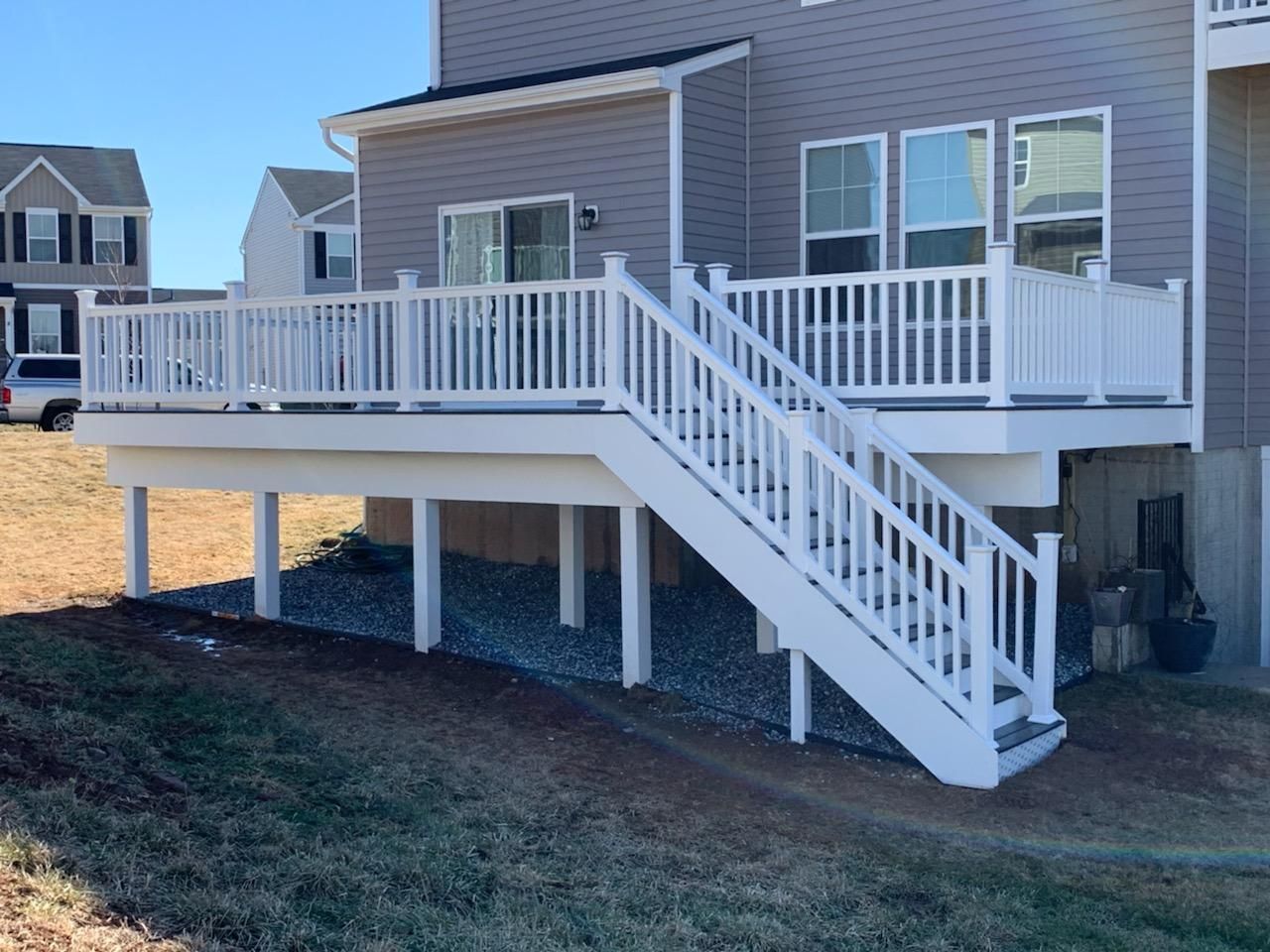 A grey house with a large white composite deck and staircase, overlooking a gravel-covered area and a sloped yard.
