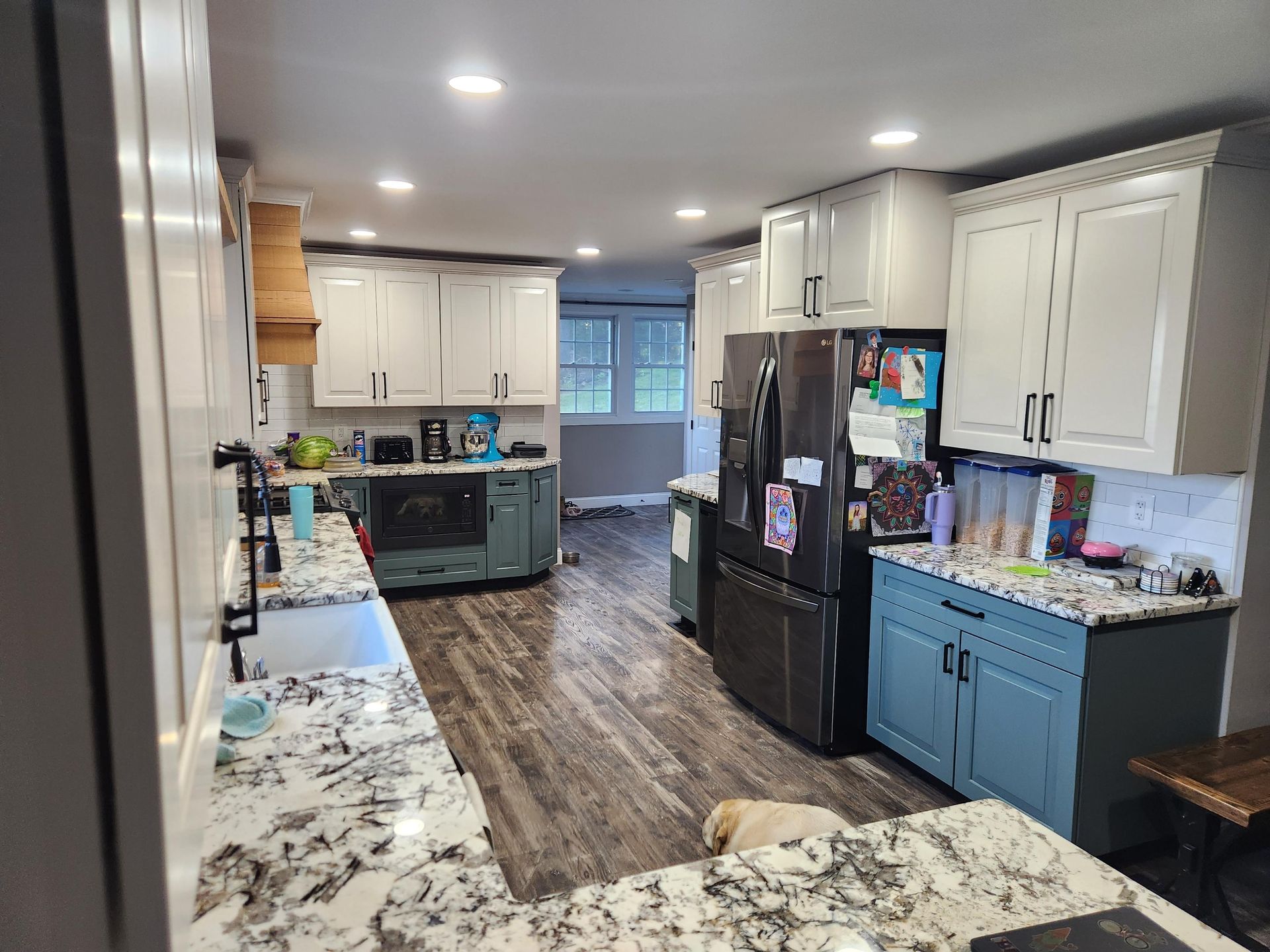 A kitchen featuring white upper cabinets, blue base cabinets, speckled granite countertops, and wood-look flooring.
