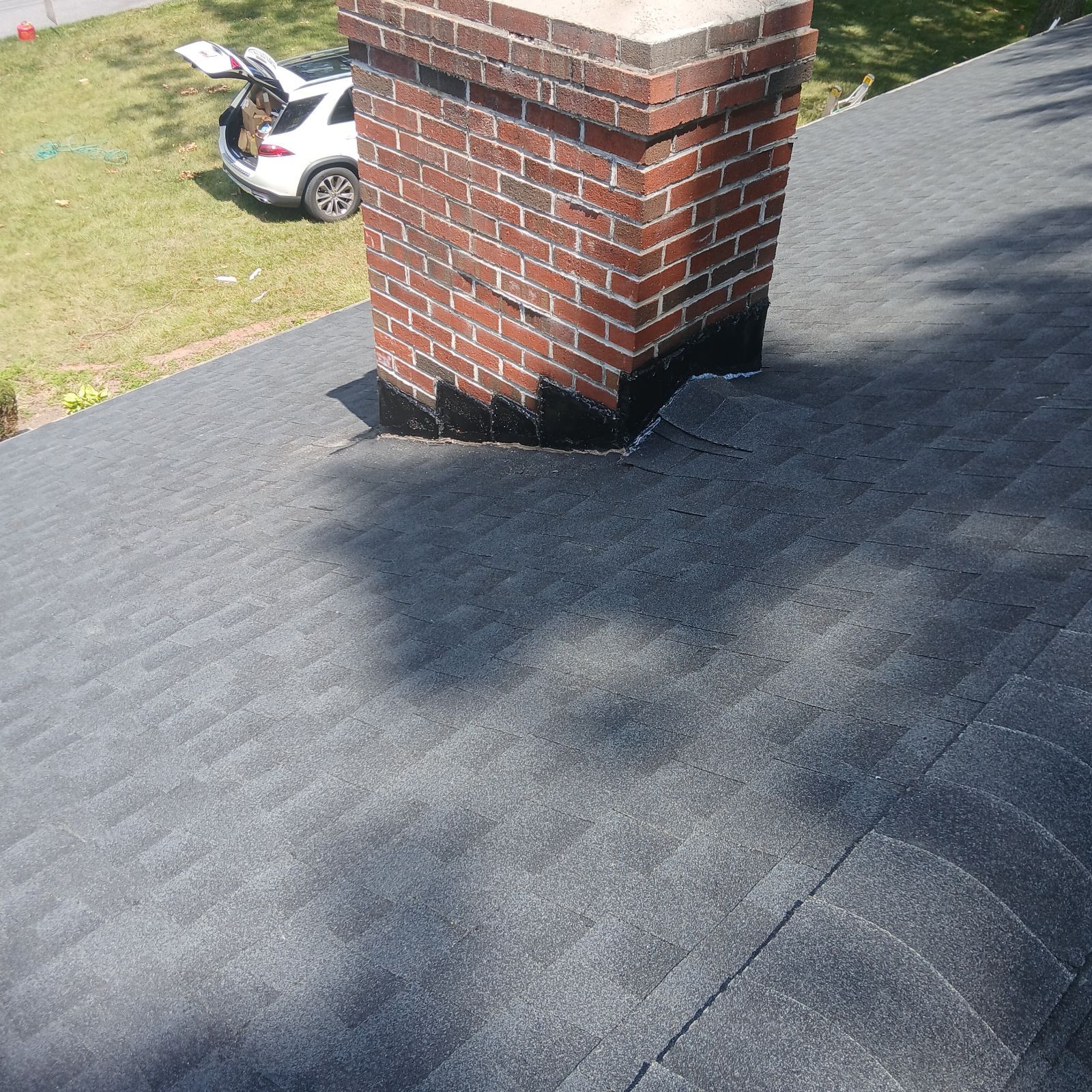 A brick chimney on a dark grey shingled roof, showing black waterproof sealant at the base.
