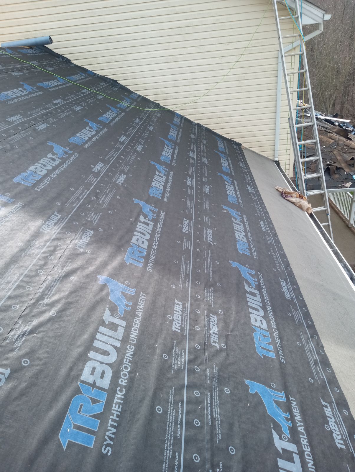 A partially shingled roof underlayment with branded synthetic material, viewed from a high angle next to an extension ladder.