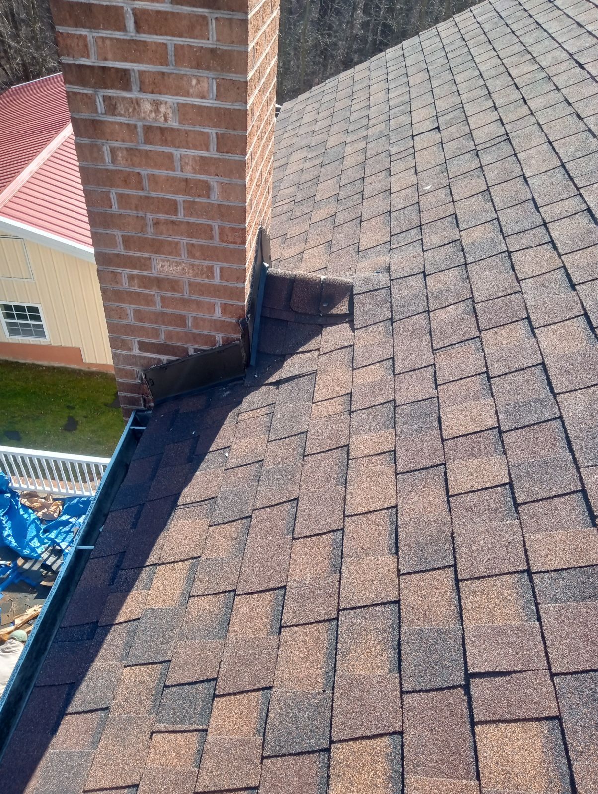 A brick chimney rising from a brown shingled roof, showing flashing details and an adjacent gutter section.